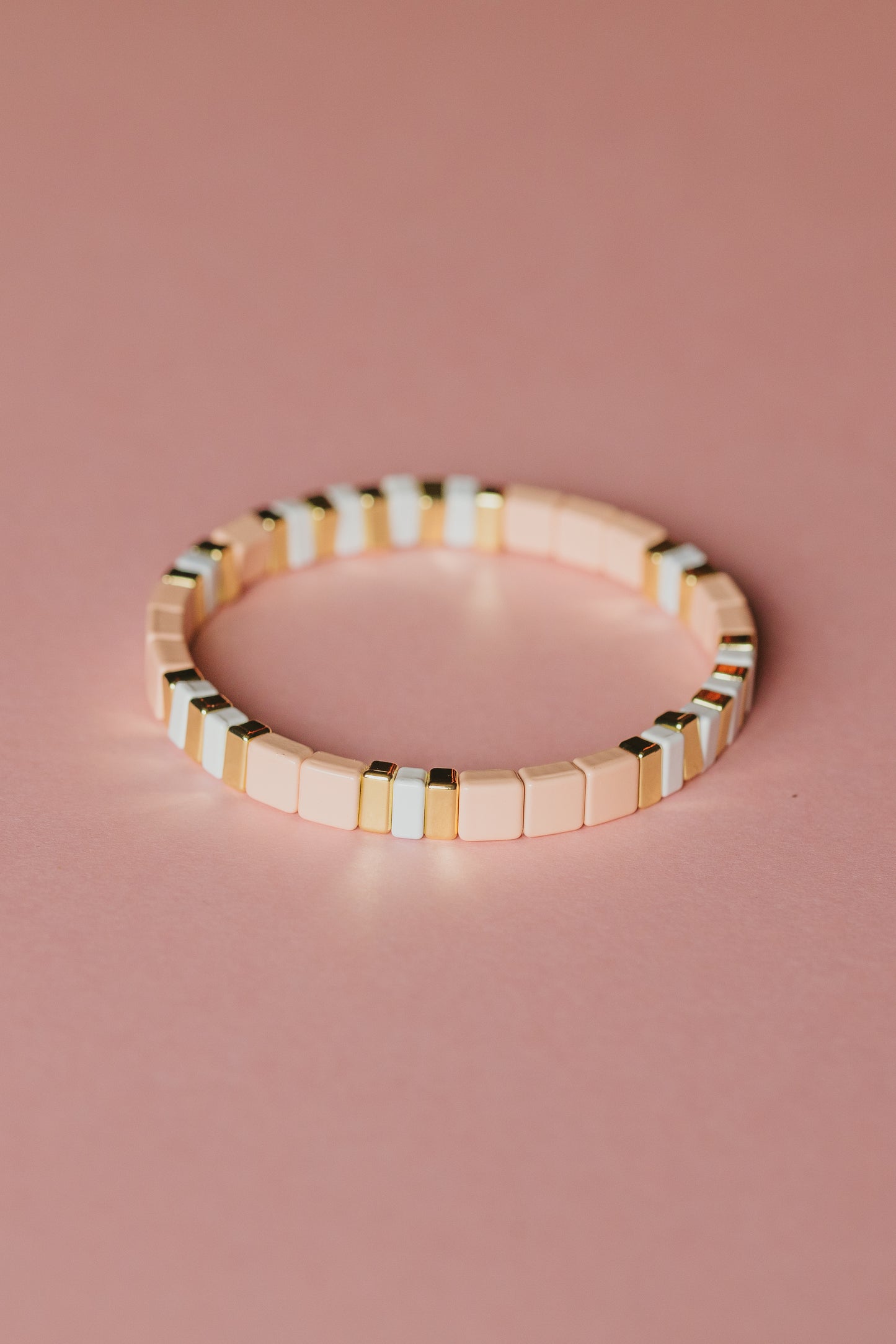 Minimalist bracelet with peach and metallic gold tiles, angled view on pink surface