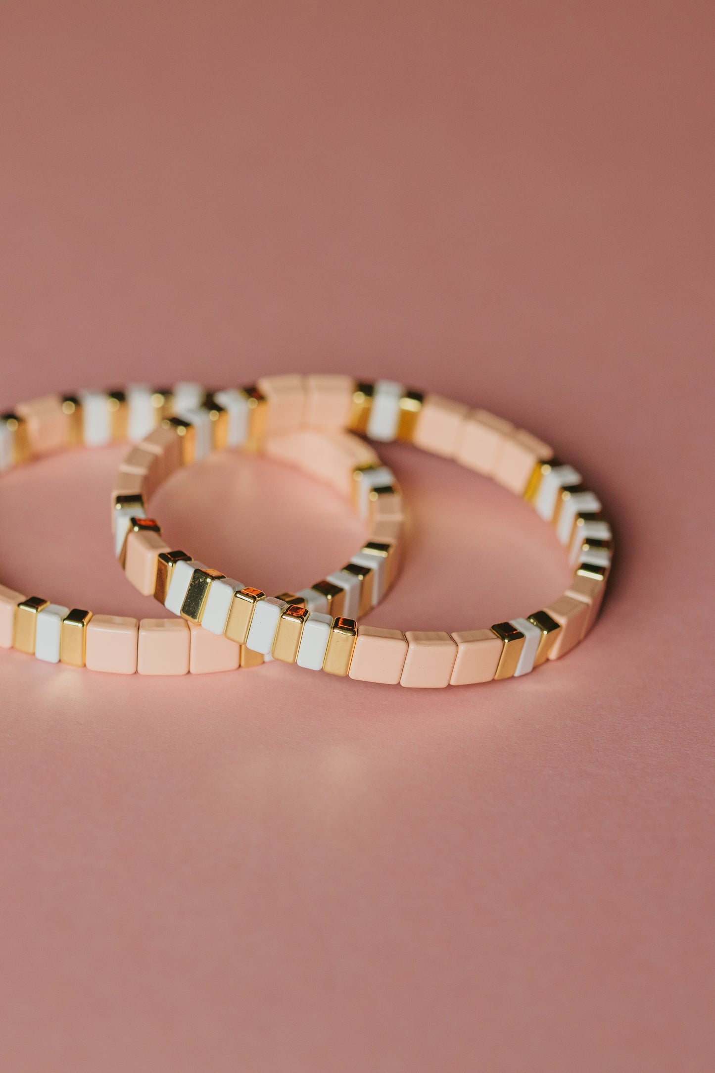 Blush pink and gold tile bracelets overlapping on pink background, modern striped pattern