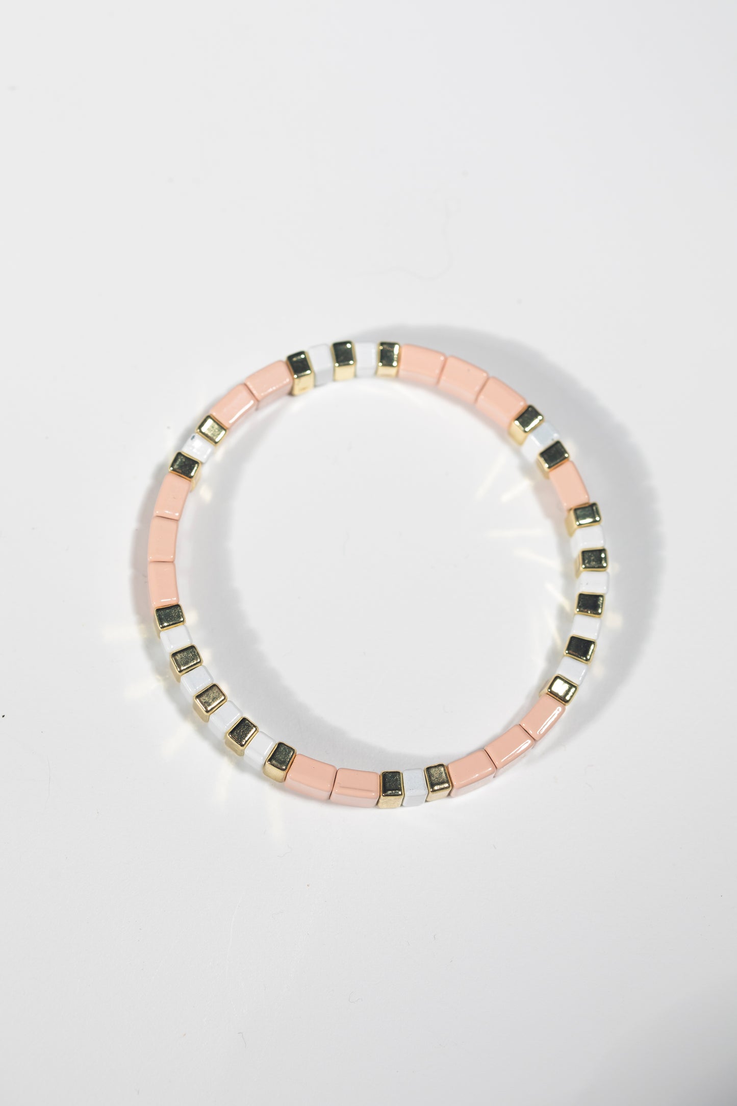 Elastic bracelet with alternating blush pink, white and gold tiles on white background