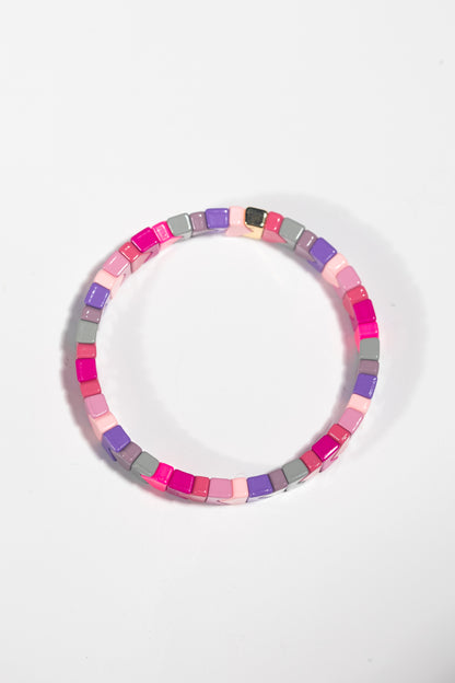 An elastic tile bracelet photographed straight-on against a white background. The bracelet is made of square tiles in a pastel and bright color palette including hot pink, light pink, purple, grey, and mauve. The tiles are arranged in a seamless circle, creating a cohesive pattern.