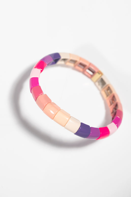 A tile bracelet photographed at an angle against a white background, featuring a gradient of colors transitioning from hot pink and purple to soft nude and cream tones. The rectangular tiles are arranged in a circle, and the angled perspective creates a dynamic sense of depth and movement. The glossy finish of the tiles gives them a luminous quality, and a distinct shadow is cast beneath the bracelet. The color progression creates a soft, feminine palette that flows smoothly from vibrant to neutral shades.