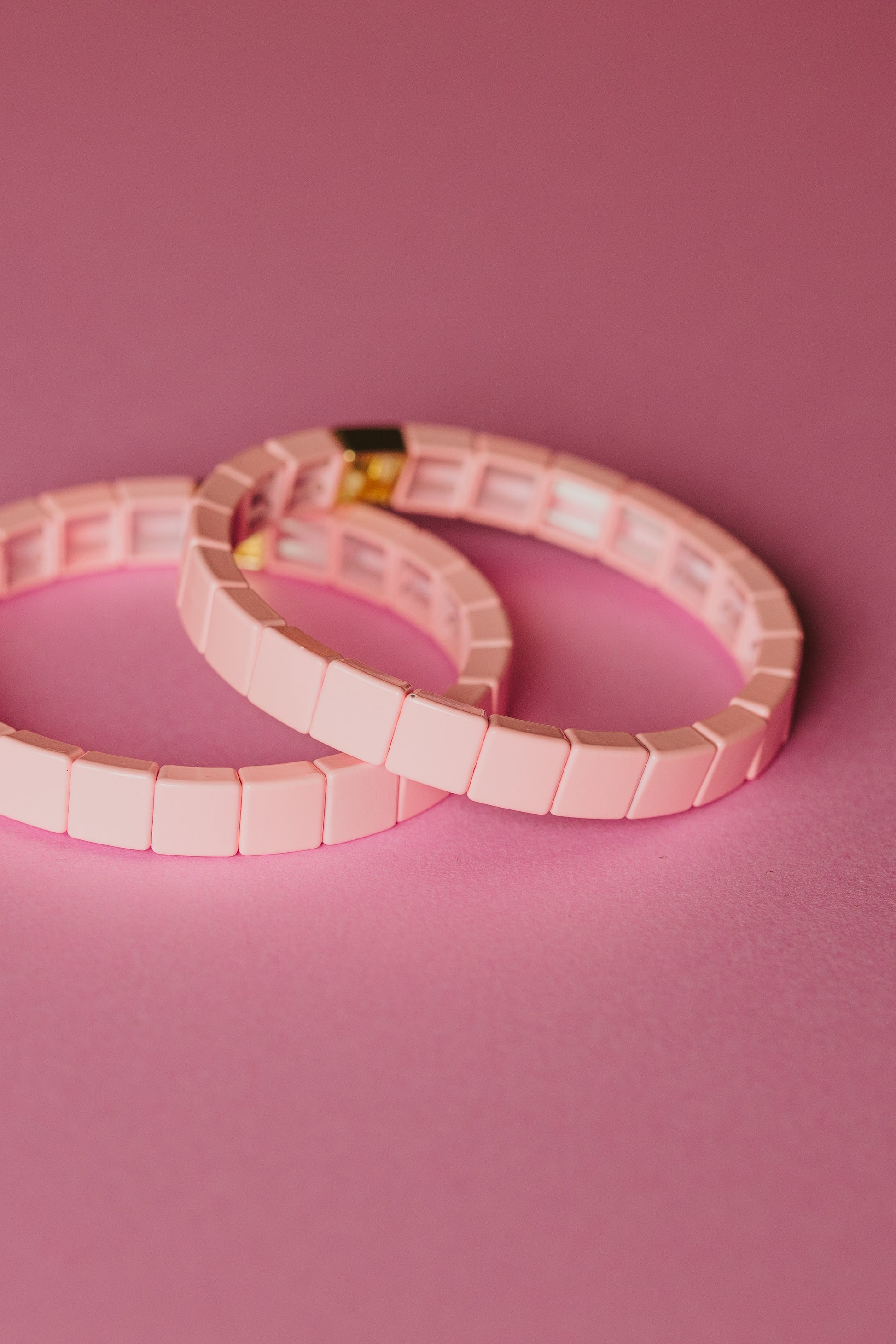 Pink tile bracelets overlapping on pink background, gold clasp detail