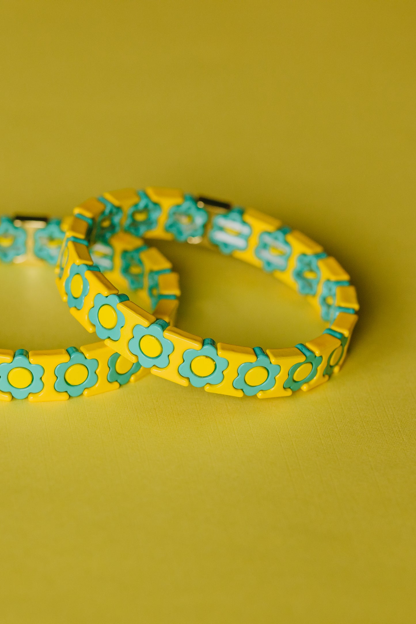 Yellow and turquoise floral bracelet set overlapping on yellow background