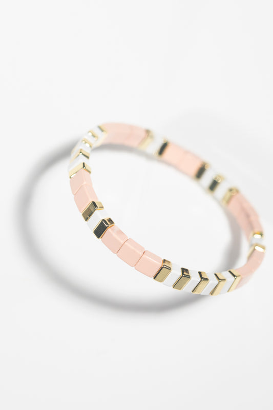 Geometric bracelet with blush and gold pattern photographed at angle, white background